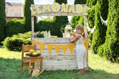 Little girl pouring natural lemonade into paper cup in park