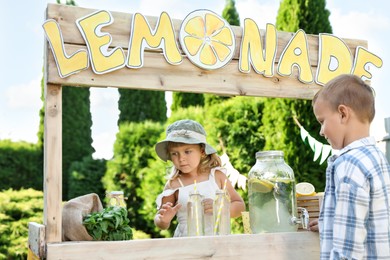 Photo of Cute little girl selling natural lemonade to boy in park