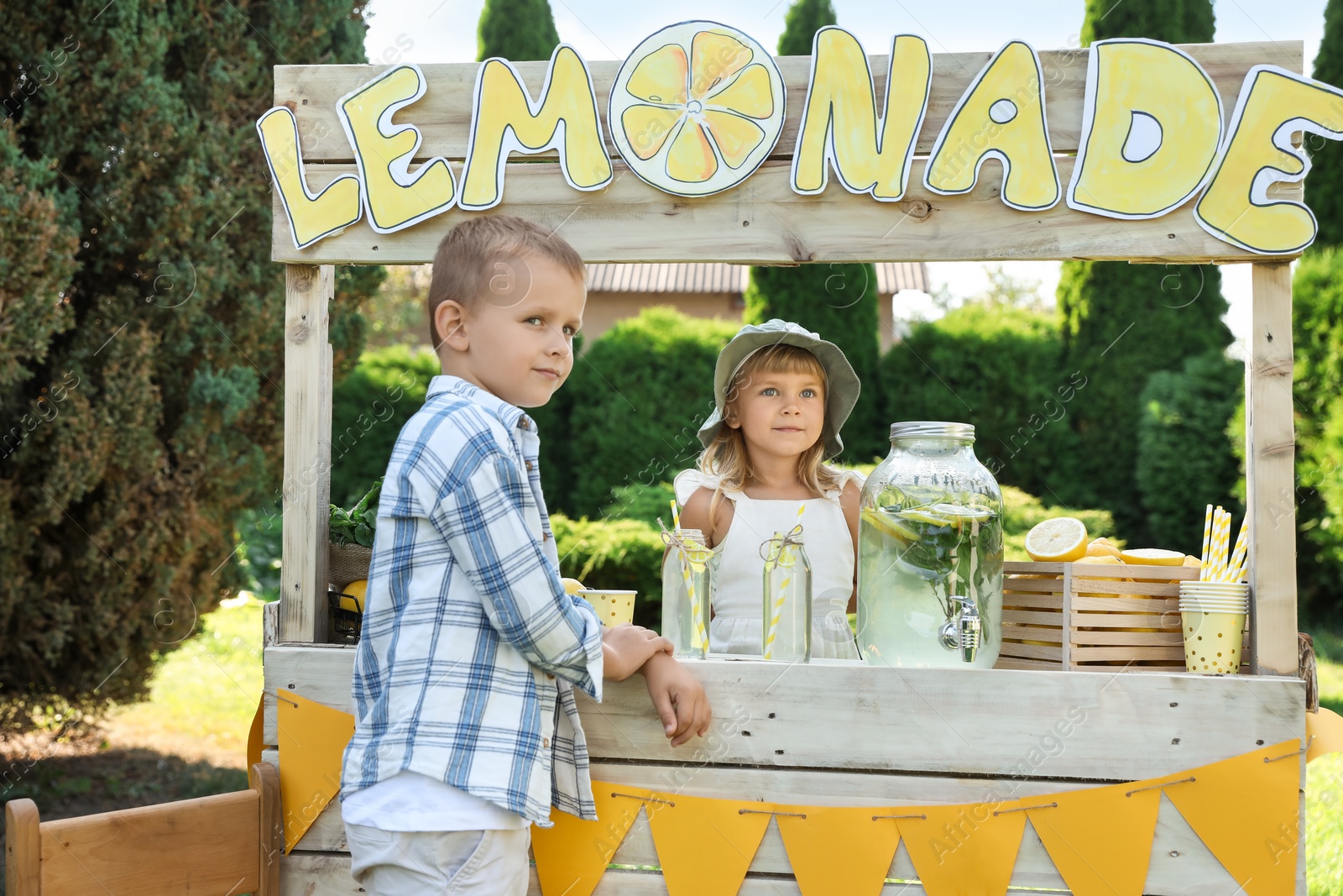 Photo of Cute little girl selling natural lemonade to boy in park