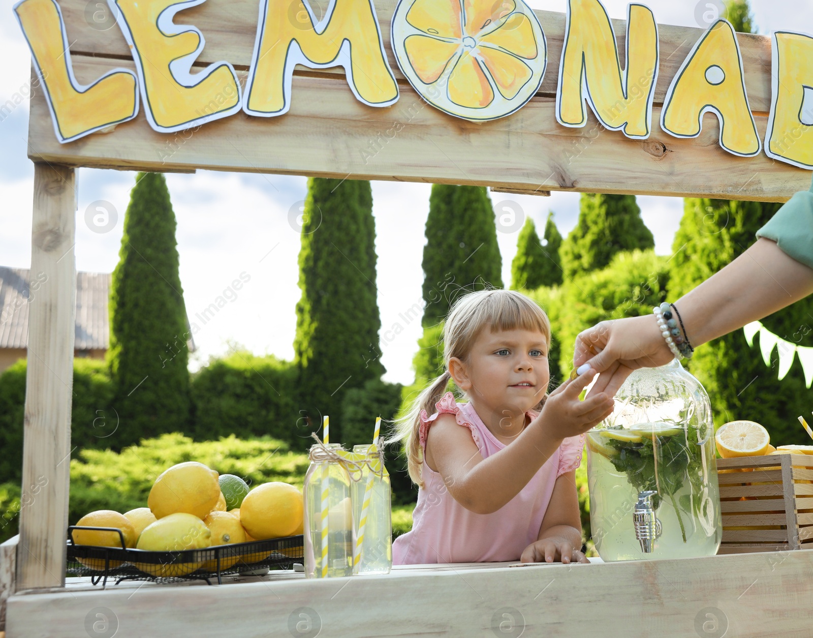 Photo of Cute little girl selling natural lemonade to woman in park