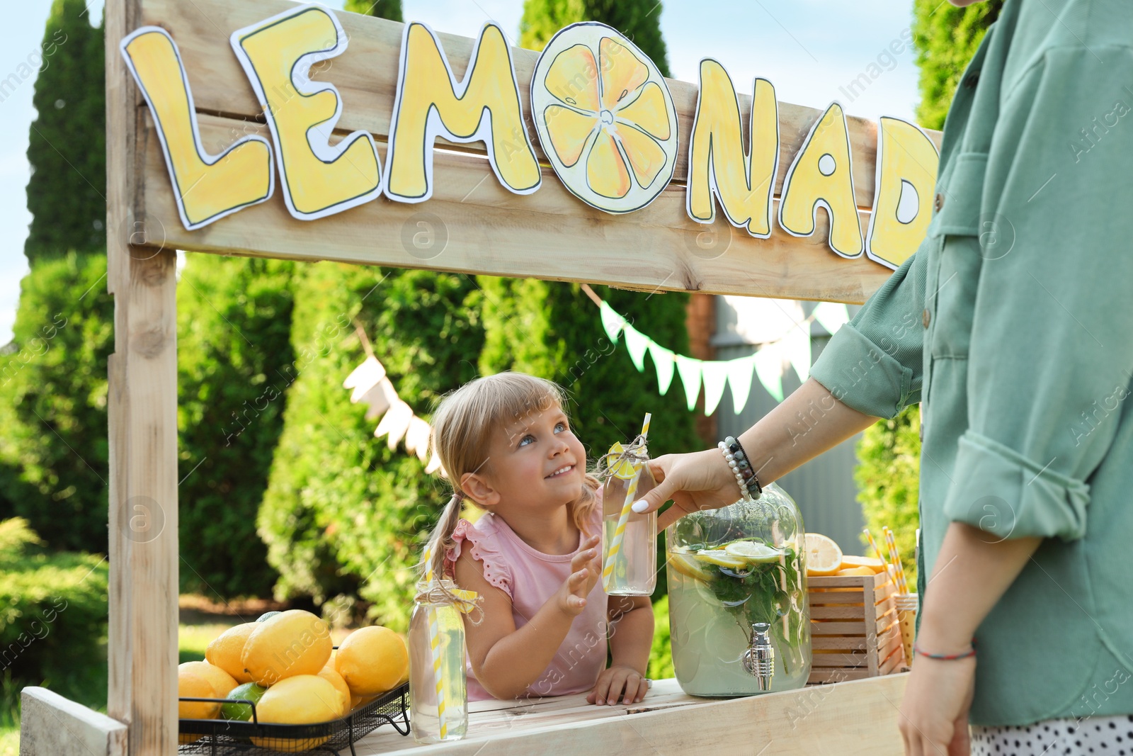 Photo of Cute little girl selling natural lemonade to woman in park