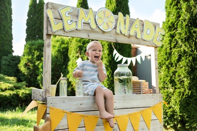 Cute little boy sitting on lemonade stand in park