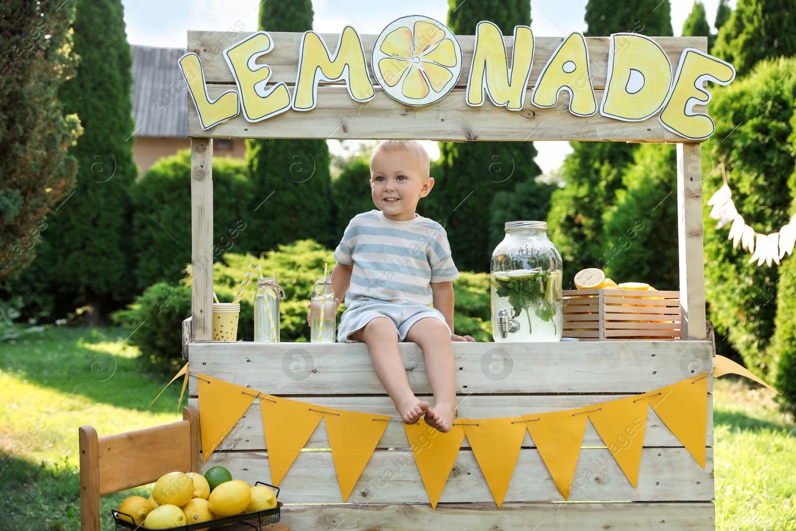 Photo of Cute little boy sitting on lemonade stand in park