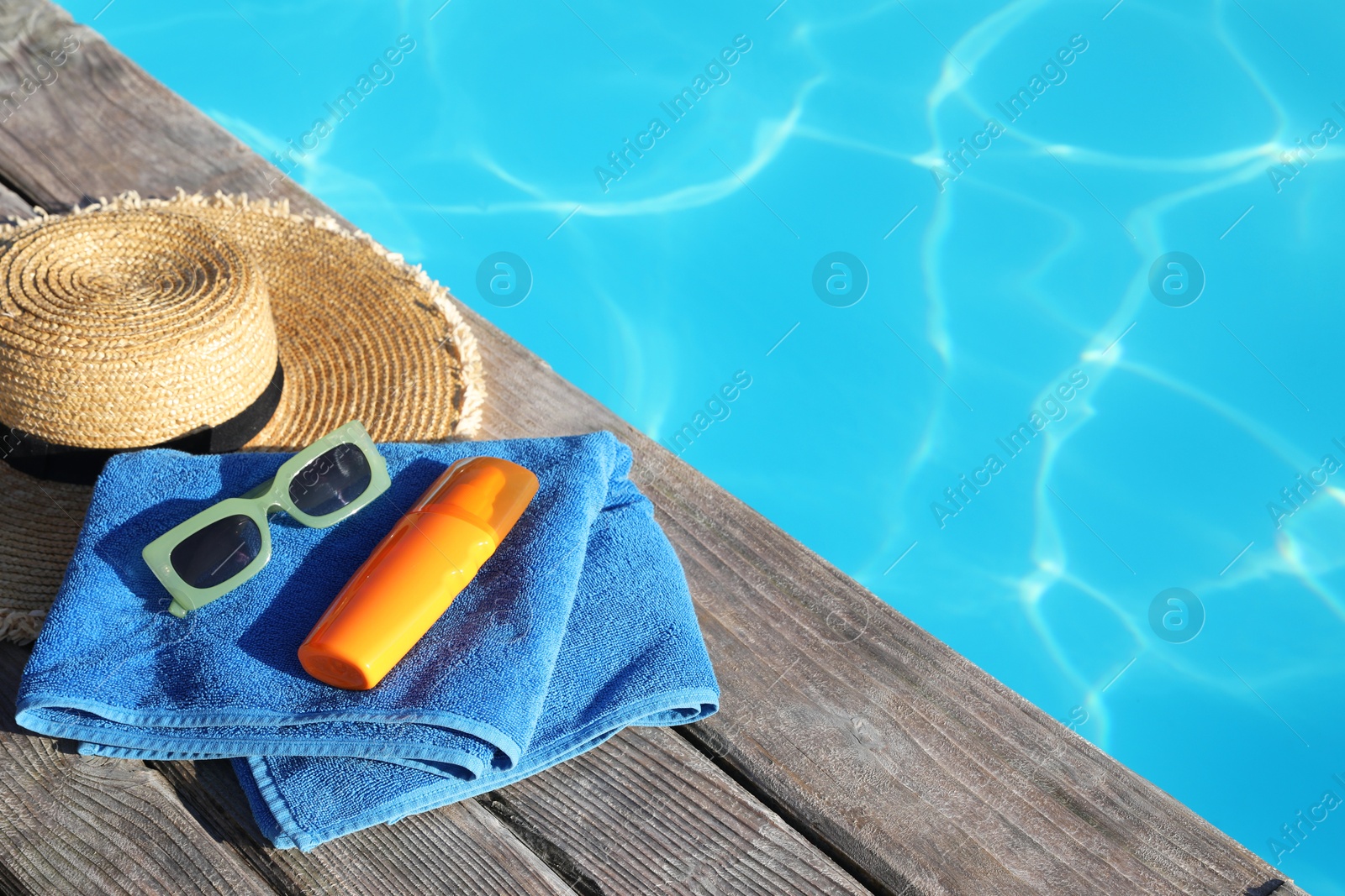 Photo of Stylish sunglasses, towel, hat and sunscreen near outdoor swimming pool. Space for text