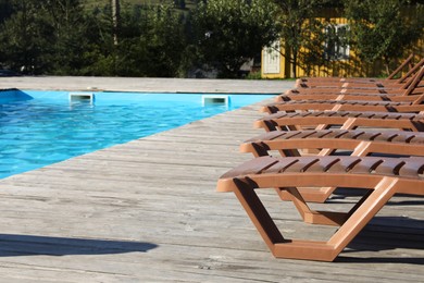 Photo of Empty sun loungers on wooden deck near outdoor swimming pool