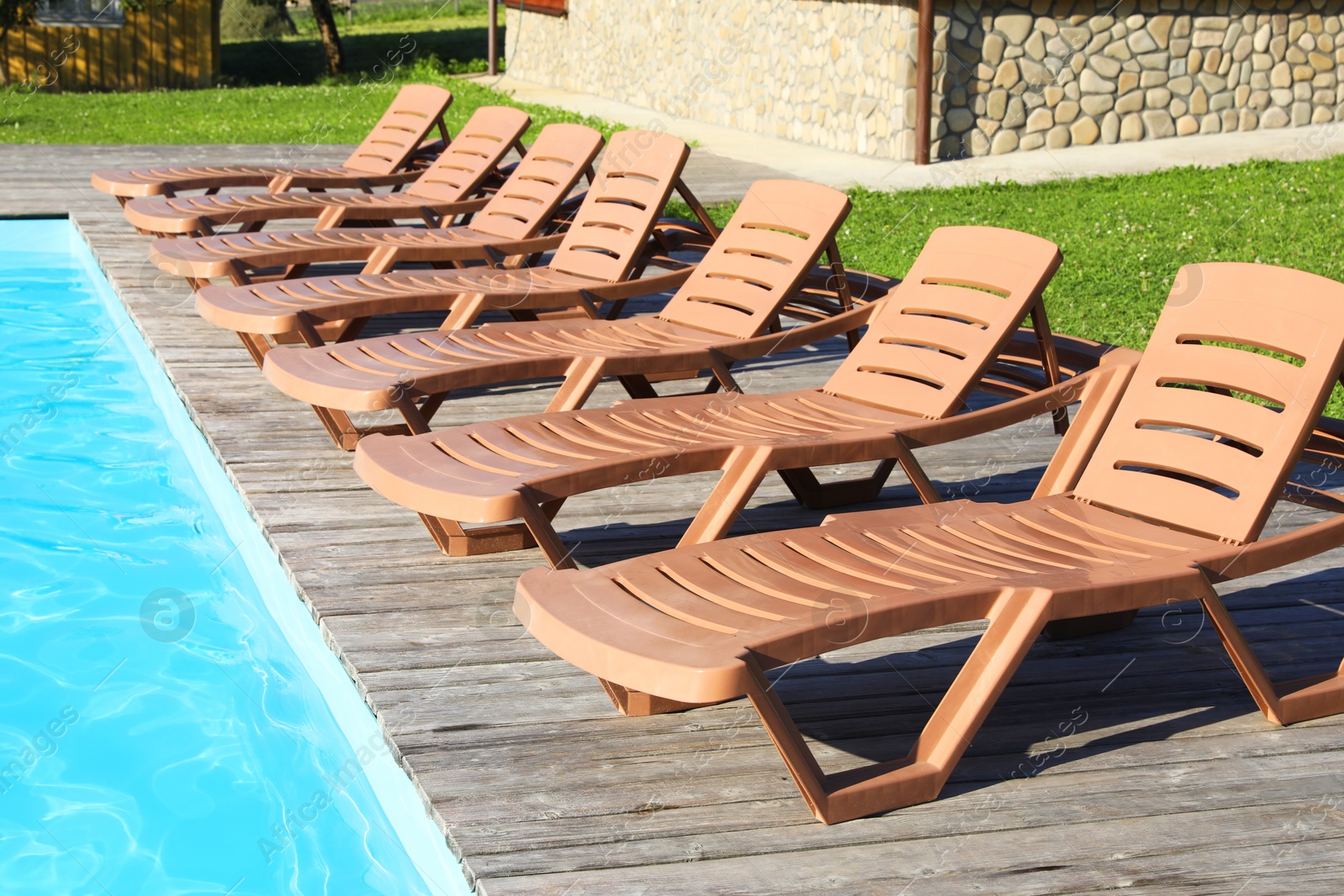 Photo of Empty sun loungers on wooden deck near outdoor swimming pool