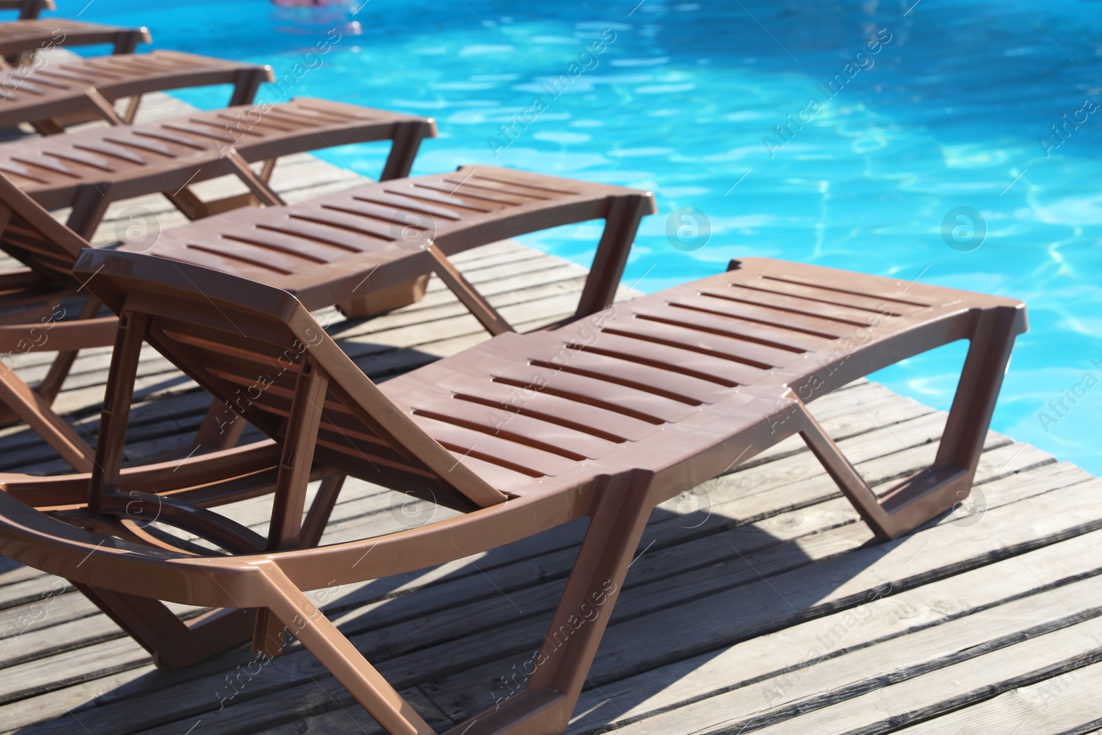 Photo of Empty sun loungers on wooden deck near outdoor swimming pool, closeup