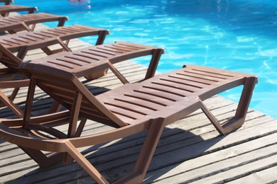 Photo of Empty sun loungers on wooden deck near outdoor swimming pool, closeup