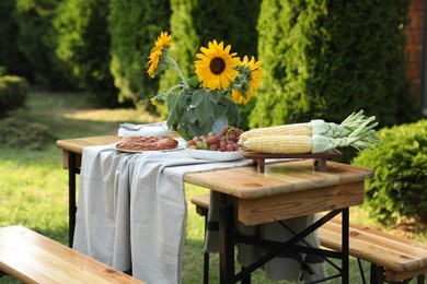 Vase with sunflowers, grapes, pie and corncobs on wooden table in garden