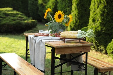 Vase with sunflowers, grapes, pie and corncobs on wooden table in garden