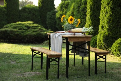 Vase with sunflowers, grapes, pie and corncobs on wooden table in garden