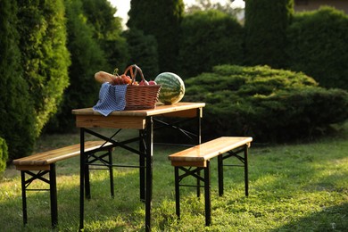 Photo of Wicker basket with grapes, baguette and watermelon on wooden table in garden