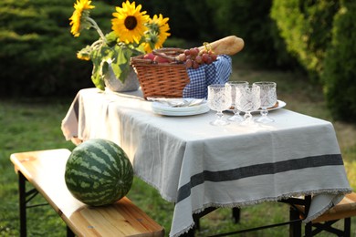 Photo of Glasses, plates, fresh products and sunflowers on table in garden