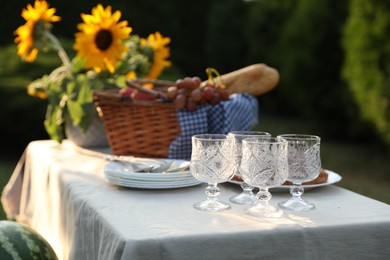 Photo of Glasses, plates, fresh products and sunflowers on table in garden, closeup