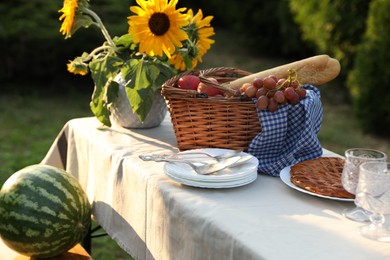 Photo of Plates, fresh products and sunflowers on table in garden