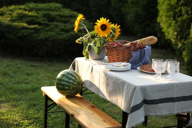 Photo of Glasses, plates, fresh products and sunflowers on table in garden