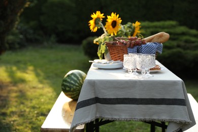 Photo of Glasses, plates, fresh products and sunflowers on table in garden