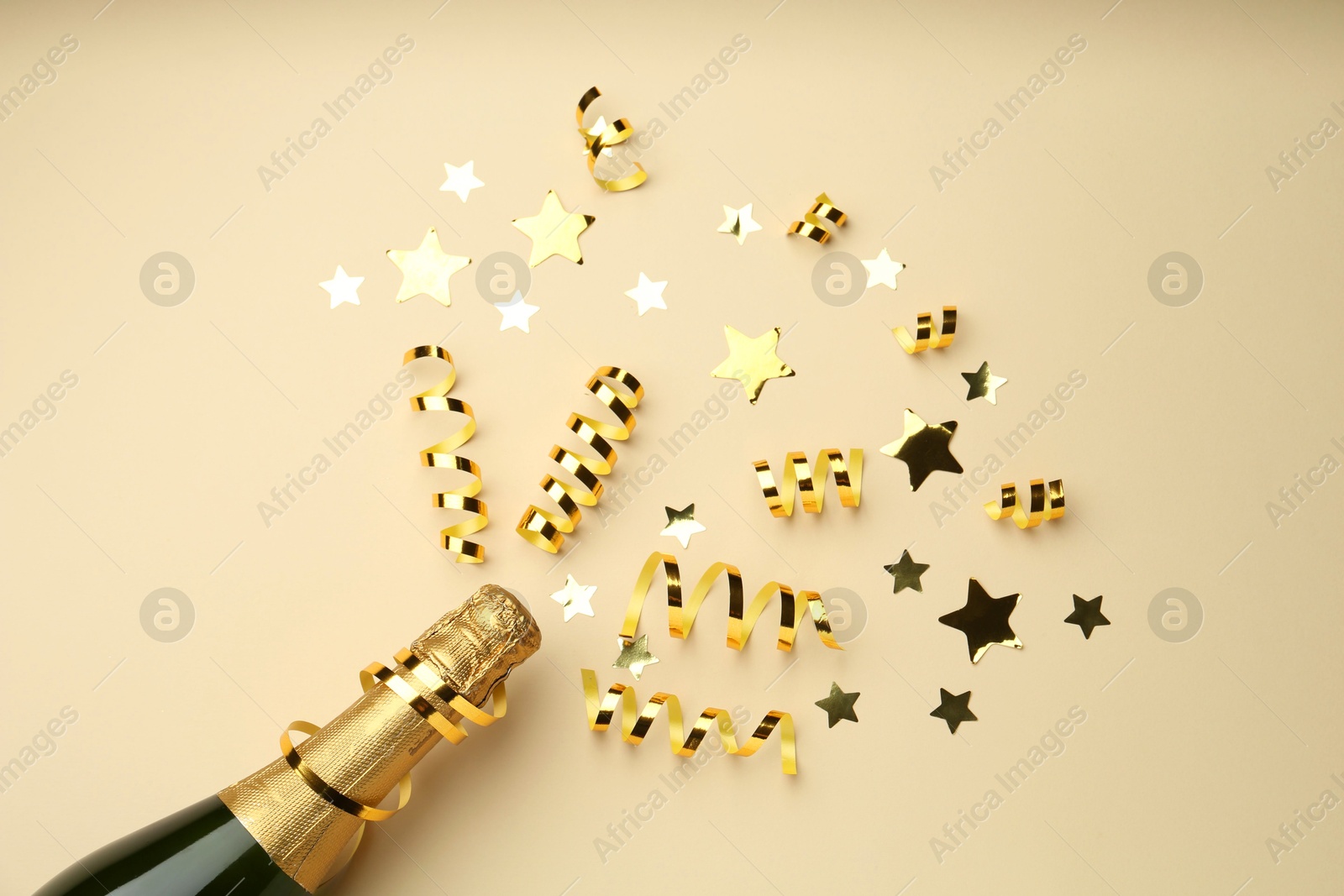 Photo of Confetti and bottle of sparkling wine on beige background, flat lay. Christmas decor