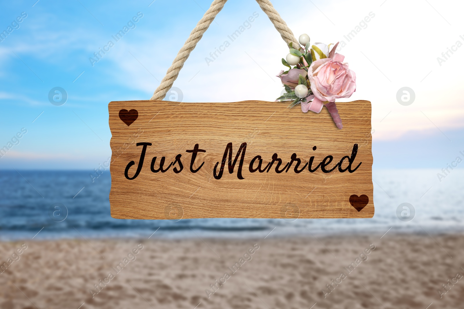 Image of Honeymoon. Wooden board with words Just Married and flowers on sandy seashore