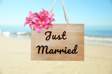 Image of Honeymoon. Wooden board with words Just Married and flowers on sandy seashore