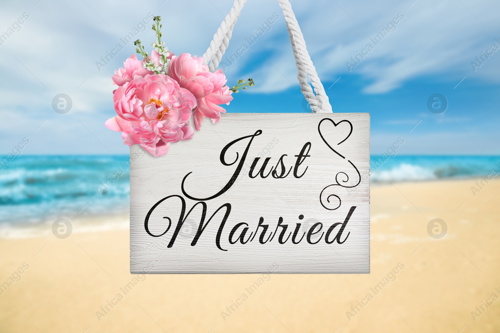 Image of Honeymoon. White wooden board with words Just Married and flowers on sandy seashore