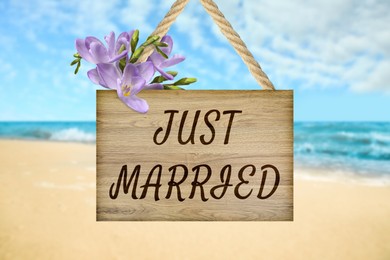 Image of Honeymoon. Wooden board with words Just Married and flowers on sandy seashore