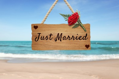 Image of Honeymoon. Wooden board with words Just Married and boutonniere on sandy seashore