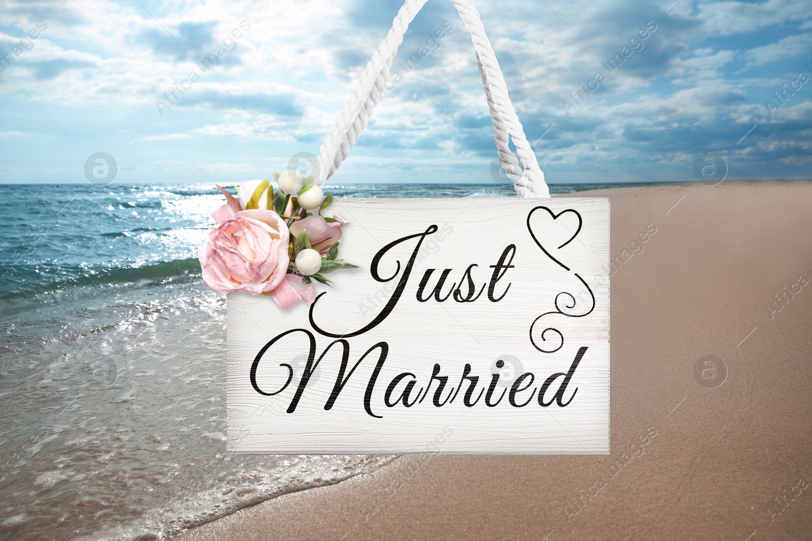 Image of Honeymoon. White wooden board with words Just Married and flowers on sandy seashore