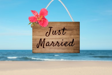 Image of Honeymoon. Wooden board with words Just Married and flower on sandy seashore