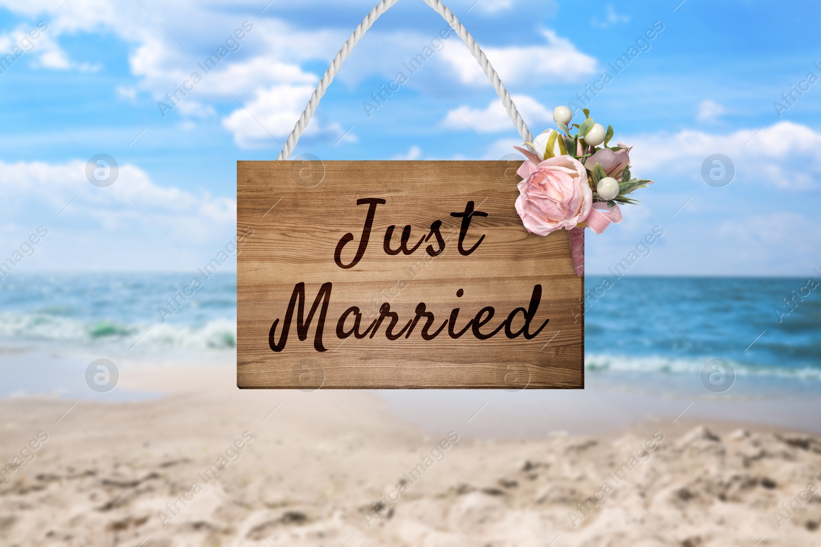 Image of Honeymoon. Wooden board with words Just Married and flowers on sandy seashore