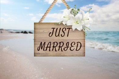 Image of Honeymoon. Wooden board with words Just Married and flowers on sandy seashore