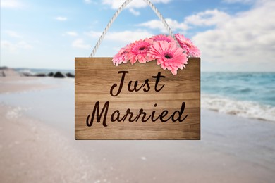 Image of Honeymoon. Wooden board with words Just Married and flowers on sandy seashore