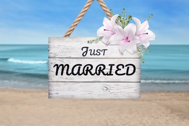 Image of Honeymoon. White wooden board with words Just Married and flowers on sandy seashore