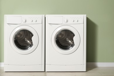 Two washing machines near light green wall