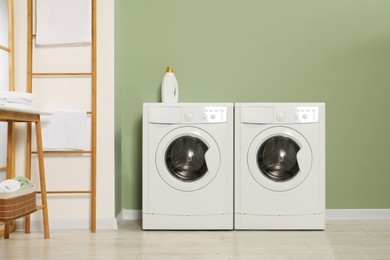 Two washing machines near light green wall in laundry room