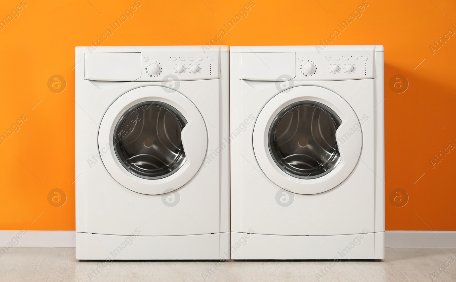 Image of Two modern washing machines near orange wall