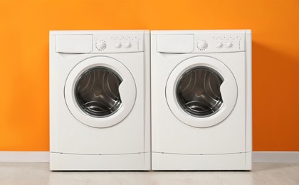 Two modern washing machines near orange wall