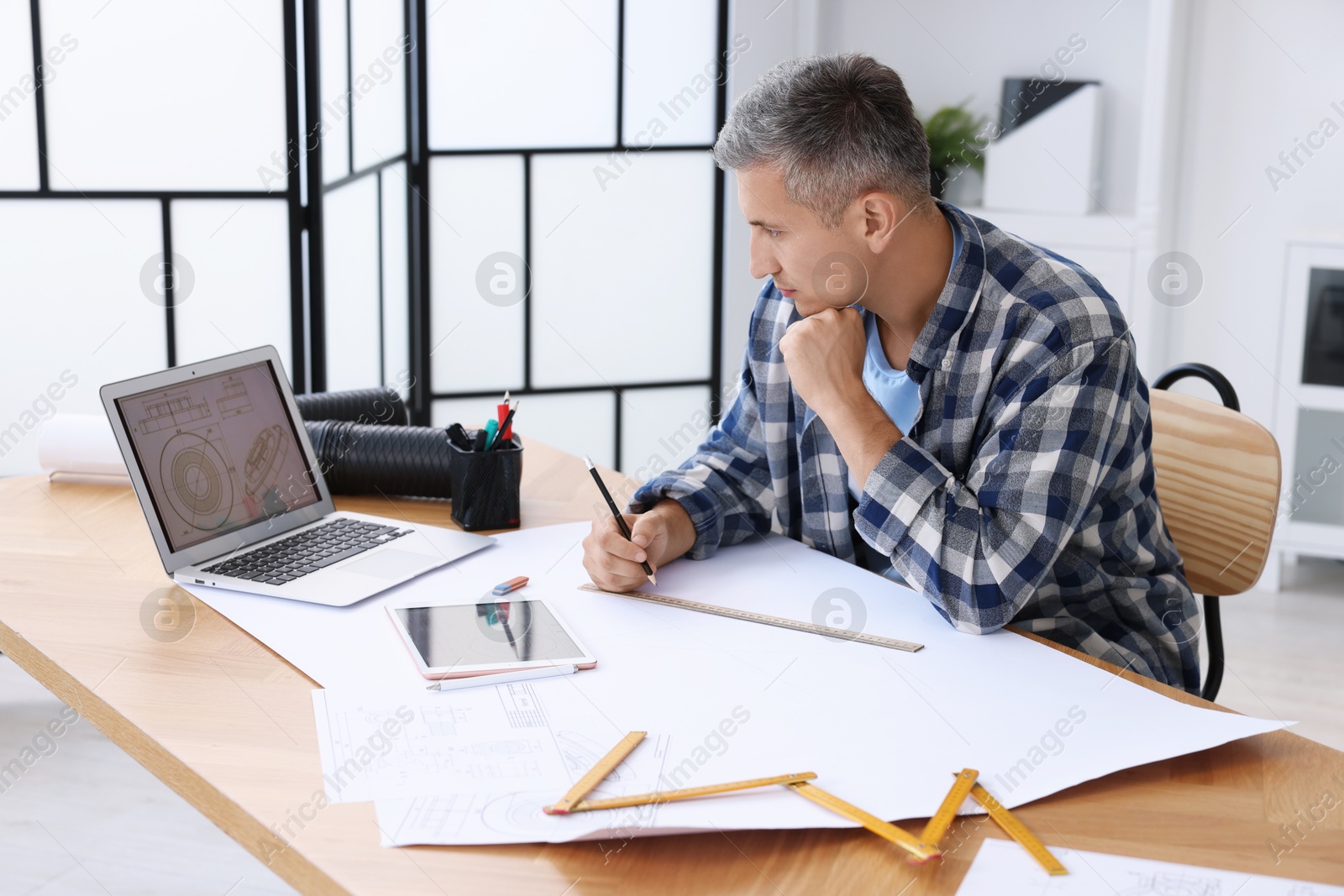 Photo of Architect making engineering drawing at wooden table in office