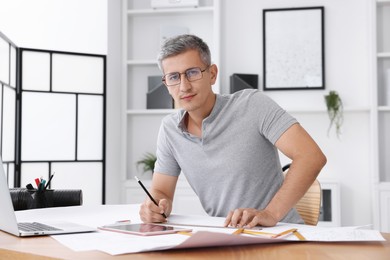 Photo of Architect with engineering drawing at wooden table in office