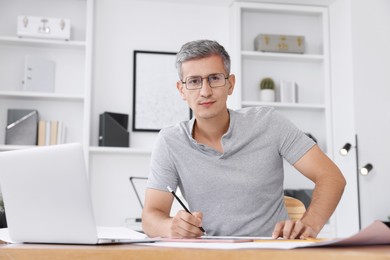 Photo of Architect with engineering drawing at wooden table in office