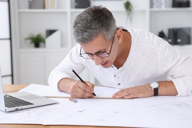 Architect making engineering drawing at wooden table in office