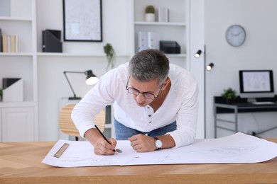 Architect making engineering drawing at wooden table in office