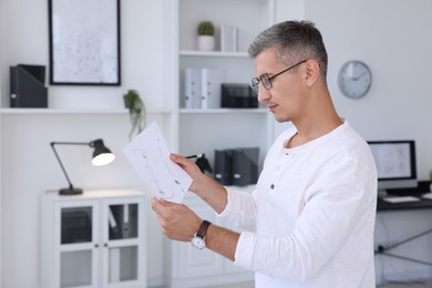 Architect holding paper sheet with engineering drawing in office