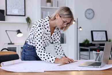 Architect making engineering drawing at wooden table in office