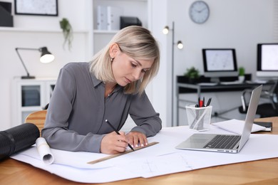 Architect making engineering drawing at wooden table in office