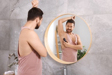 Smiling man applying roll-on deodorant near mirror at home