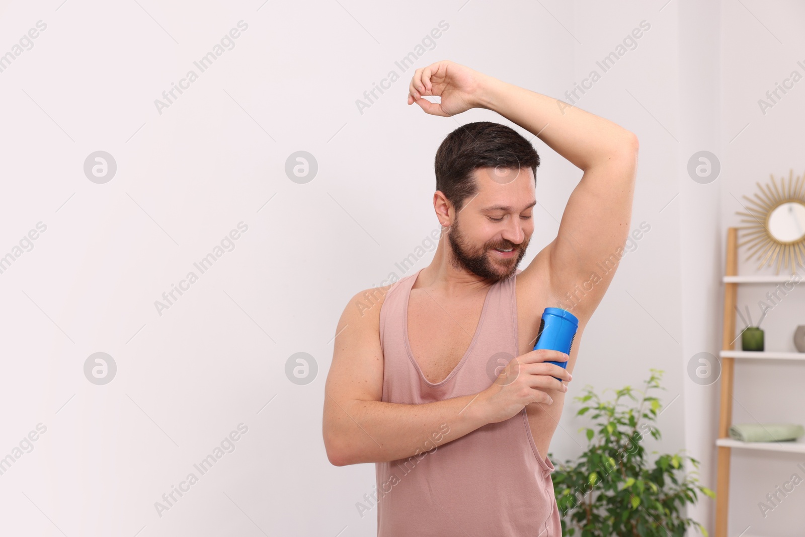 Photo of Smiling man applying solid deodorant at home. Space for text