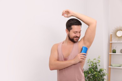 Smiling man applying solid deodorant at home. Space for text