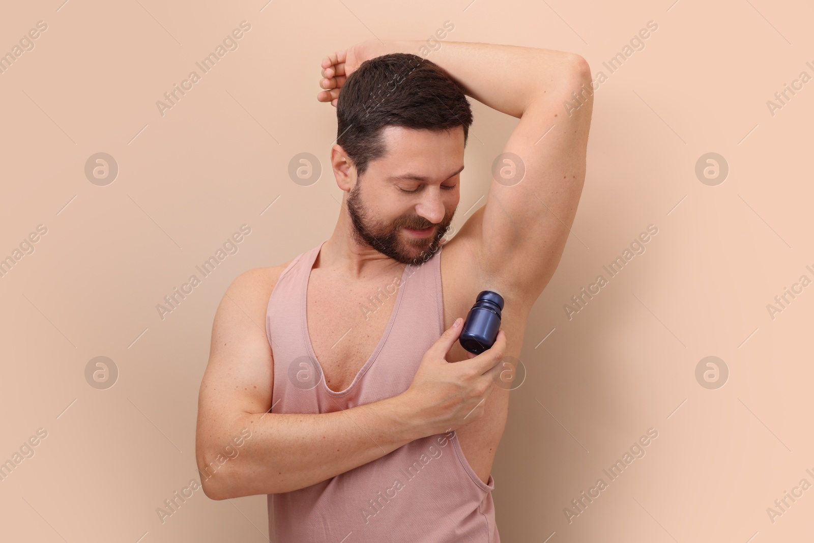 Photo of Man applying roll-on deodorant on beige background