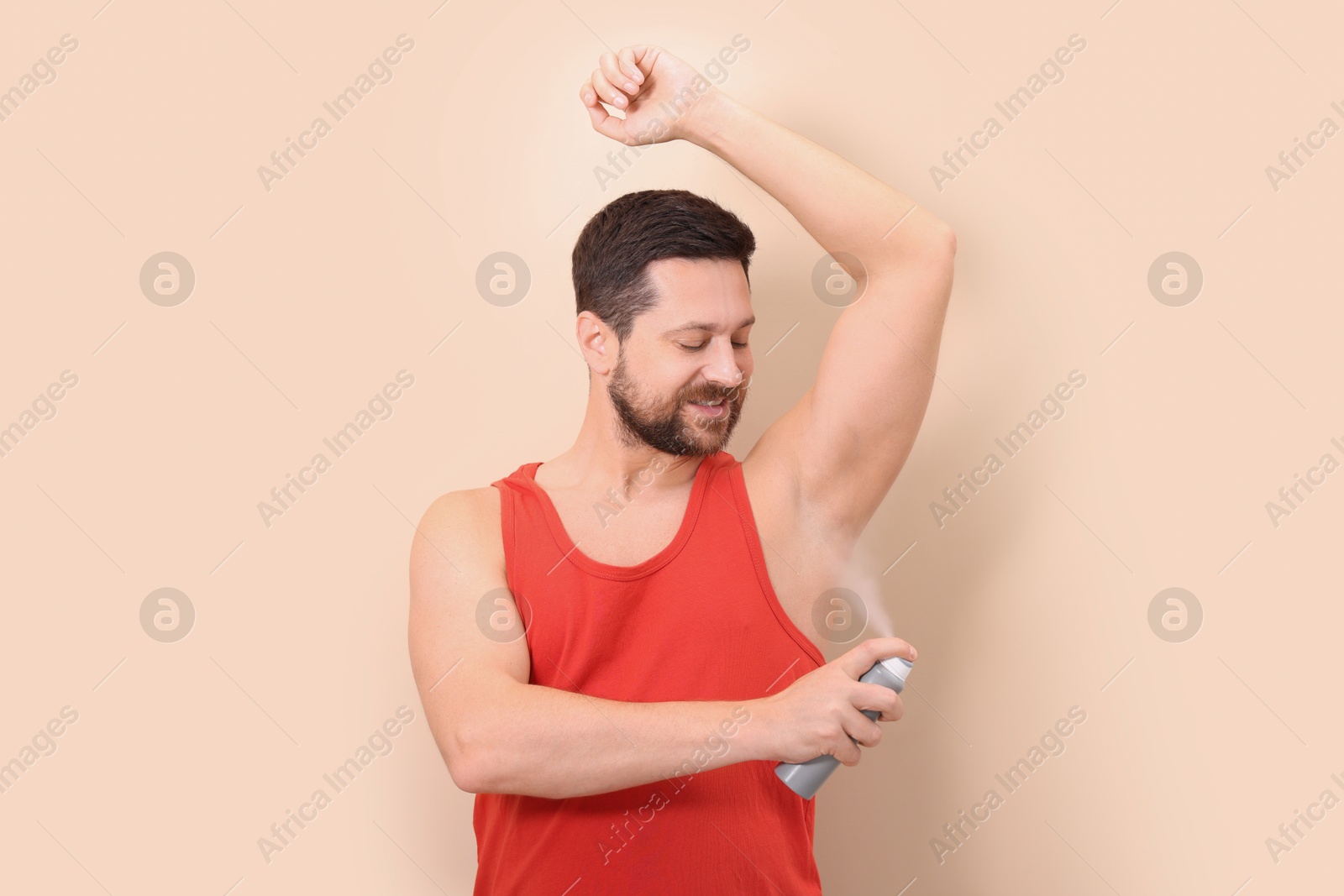 Photo of Smiling man applying spray deodorant on beige background